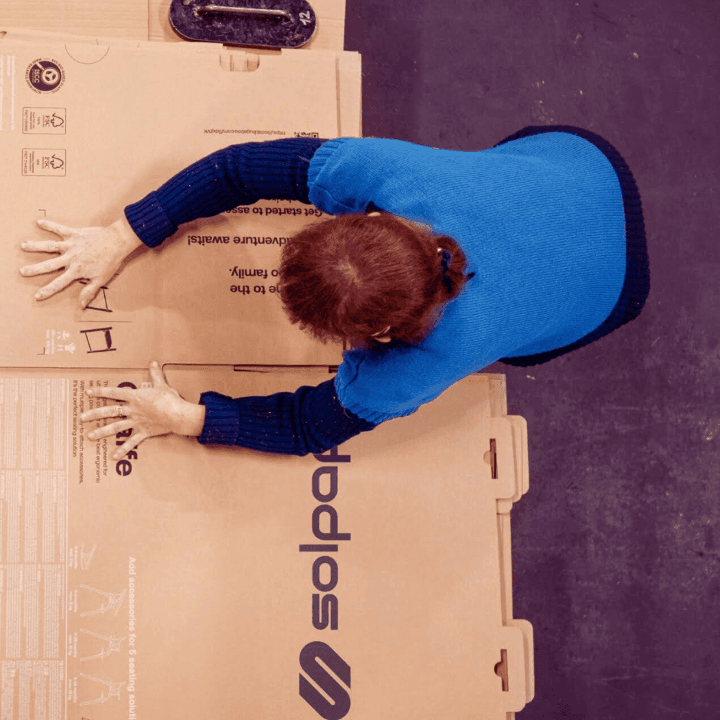 Krabice a obaly na míru: jak významně snížit logistické náklady? 9 Pracovník skládající velké kartonové obaly na podlaze průmyslové haly, zachycený z pohledu shora