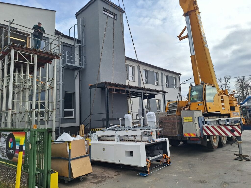 Vykládka automatického aplikátoru pásky ts-1450c3 pomocí jeřábu před výrobní halou