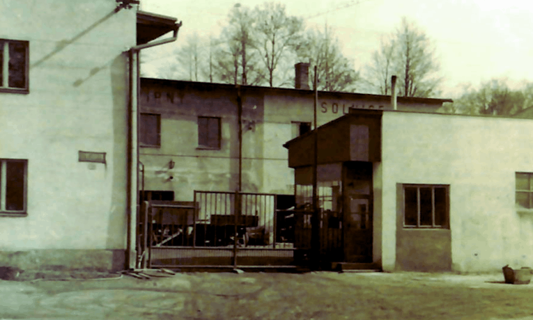 Dobová fotografie původního areálu kartonážky solpap v solnici se zavřenou kovovou branou a vrátnicí